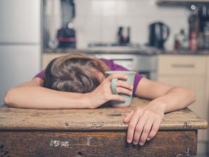 Girl sleeping at kitchen table with coffee in hand